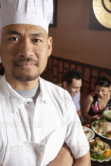 Asian male chef with diners in background