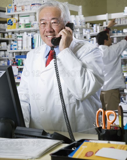 Senior Asian pharmacist talking on telephone