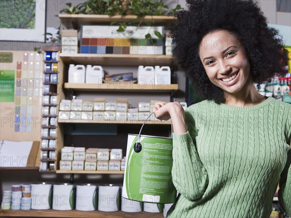 African woman holding paint can in store