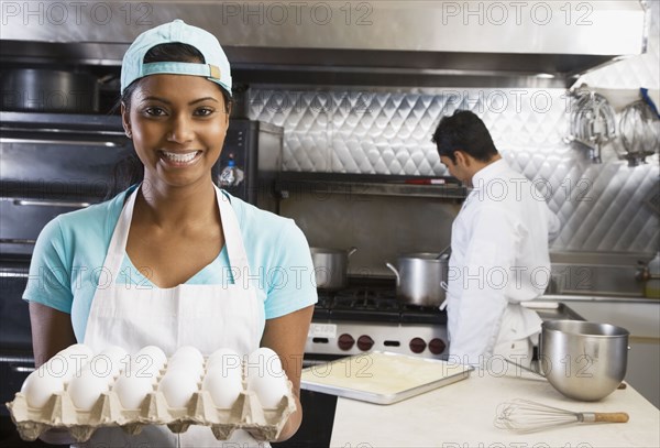 Mixed Race female kitchen worker holding eggs