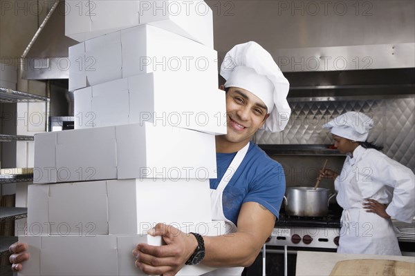 Hispanic male pastry chef carrying stack of boxes