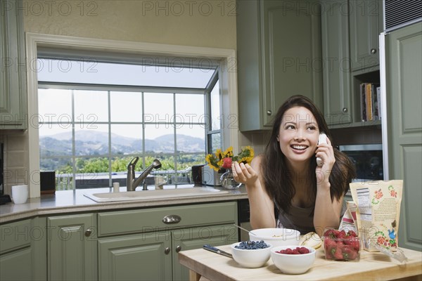 Woman eating cereal and talking on telephone in morning