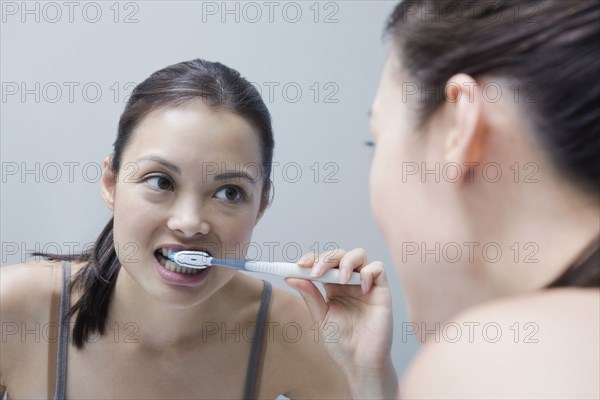 Woman brushing teeth in mirror