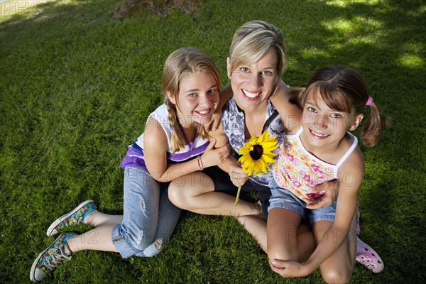 Caucasian mother and daughters sitting grass