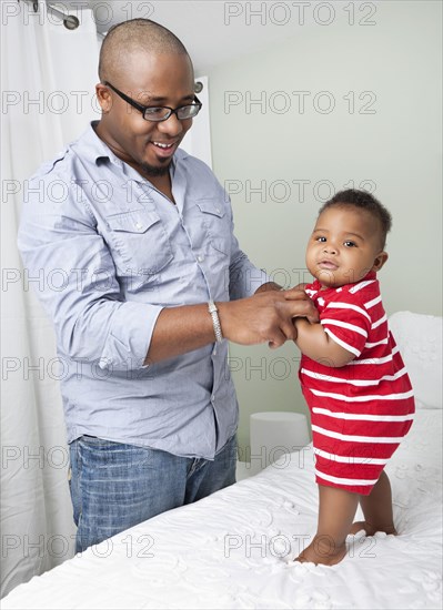 African American father helping baby son to stand up