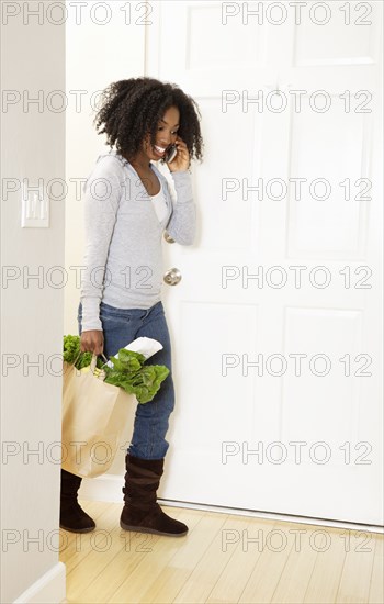 African American woman carrying bag of groceries and talking on cell phone
