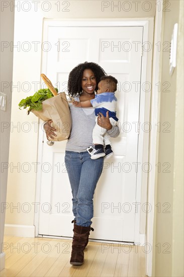 African American woman carrying bag of groceries and baby son
