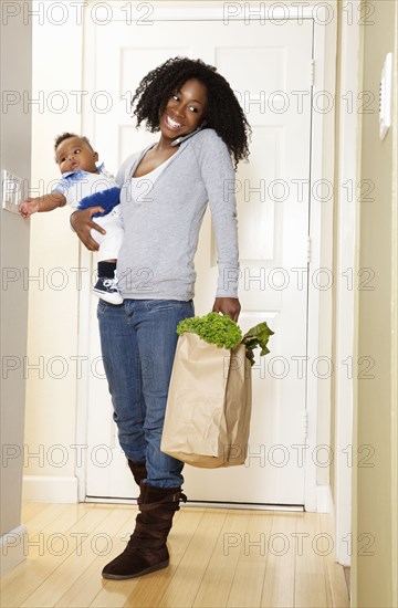 African American woman carrying bag of groceries. baby son and talking on phone