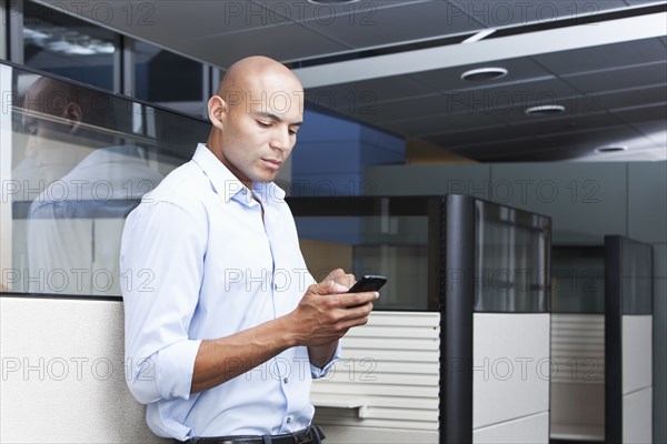 Mixed race businessman text messaging on cell phone in office