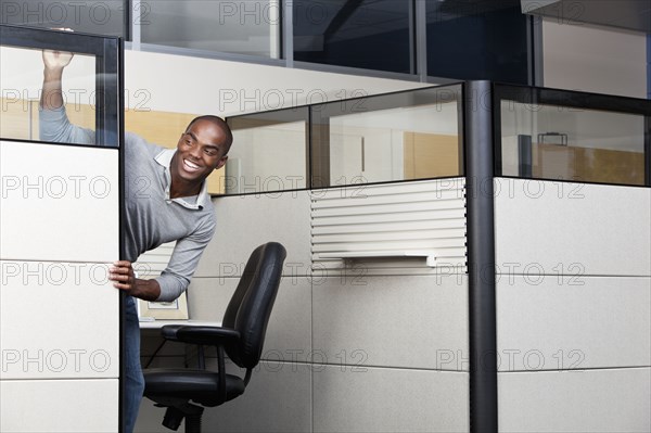 Mixed race businessman peering out from office cubicle