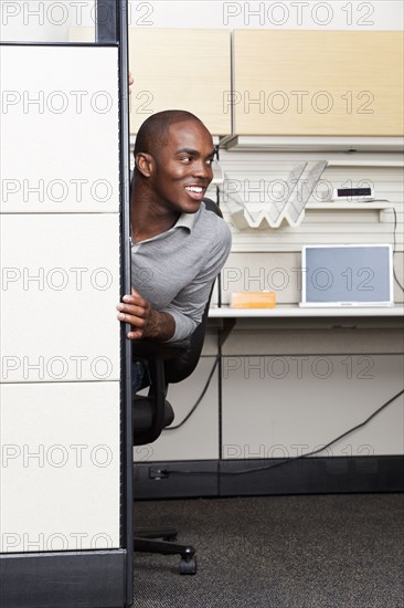 Mixed race businessman peering out from office cubicle