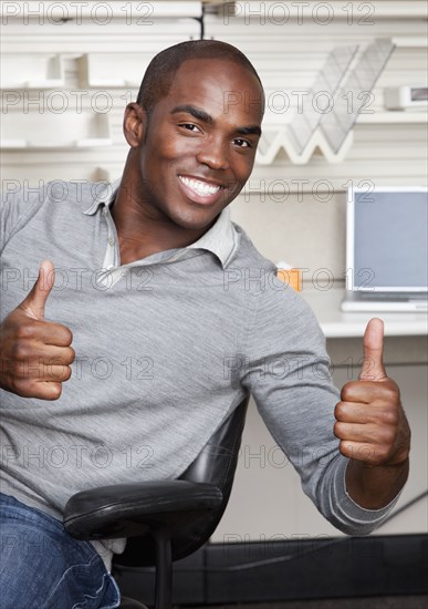 Mixed race businessman giving thumbs up in office