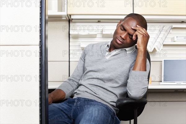 Frustrated mixed race businessman sitting in office cubicle