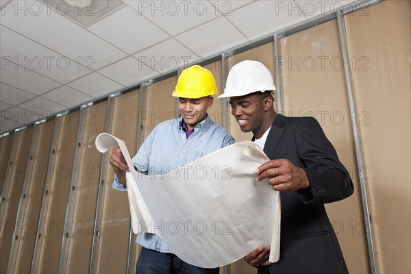 Mixed race businessmen looking at blueprints in room under construction