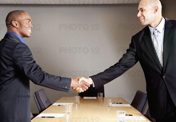 Mixed race businessmen shaking hands in conference room