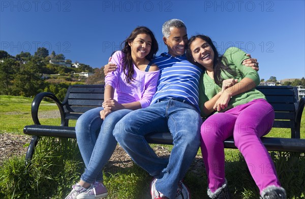 Hispanic father and daughters sitting on park bench