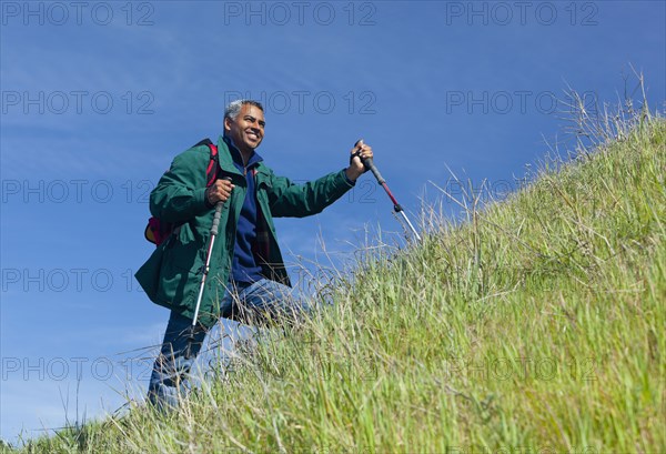 Mixed race man hiking on grassy hill