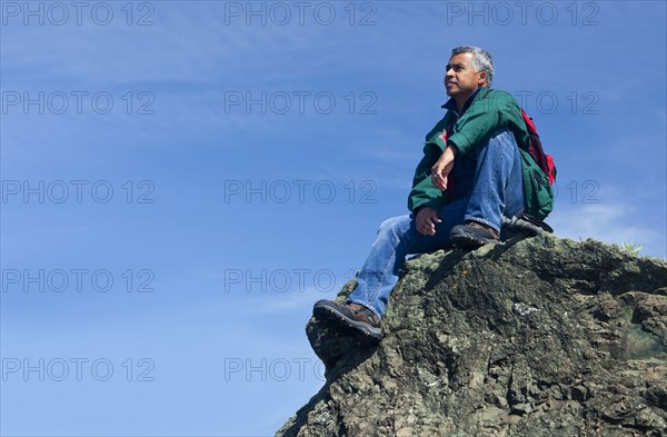 Mixed race man sitting on rocky hilltop