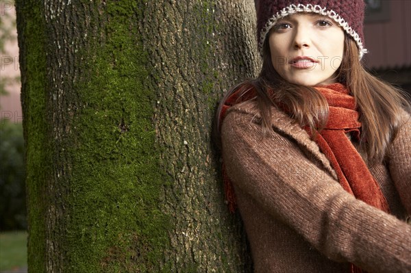 Mixed race woman leaning against tree in park