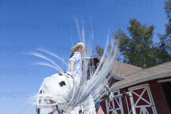 Mixed race girl riding horse on ranch