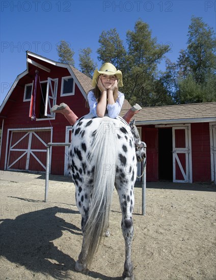 Mixed race girl laying on horse on ranch