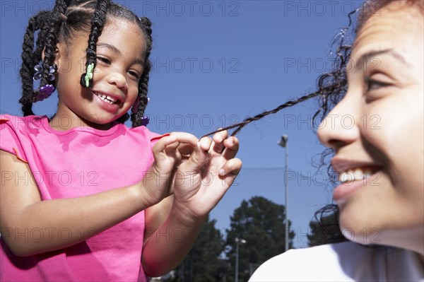 Mixed race girl braiding mother's hair