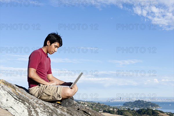 Climber using laptop on rocky hilltop