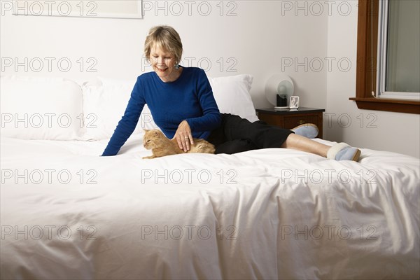 Senior Caucasian woman petting cat on bed