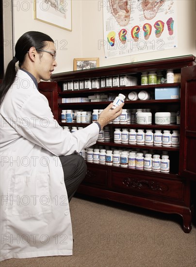 Chinese medicine practitioner selecting herbs from cabinet