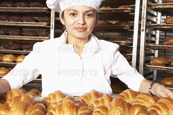 Hispanic baker carrying tray of croissants in bakery