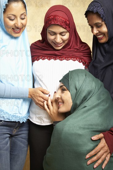 Woman in headscarf listening to friend's pregnant belly