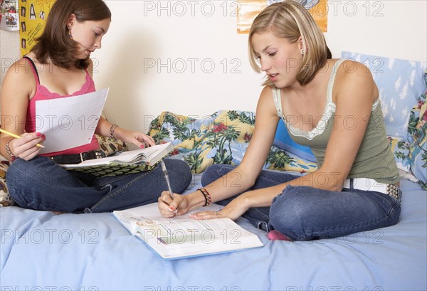 Caucasian teenage girls doing homework on bed