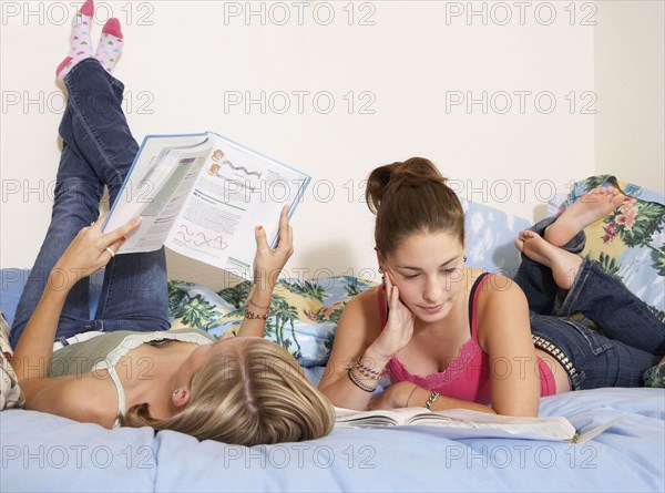 Caucasian teenage girls doing homework on bed