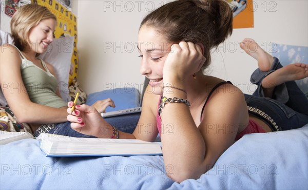 Caucasian teenage girls doing homework on bed