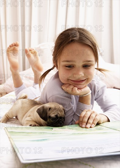 Mixed race girl reading with dog on bed