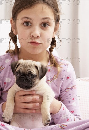 Mixed race girl holding dog on bed