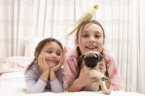 Mixed race girls with dog and bird on bed