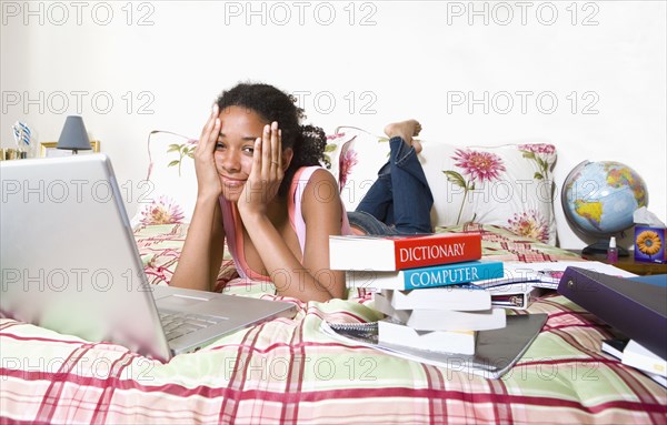 Mixed race teenage girl doing homework on bed