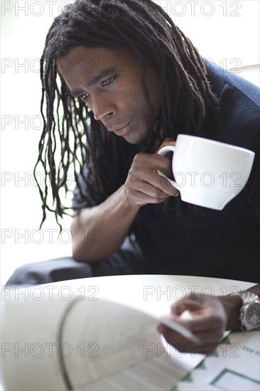 Mixed race businessman drinking coffee and reviewing report