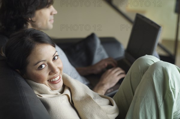 Hispanic woman wrapped in blanket on sofa