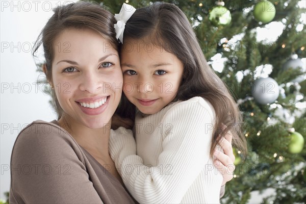 Hispanic mother and daughter hugging next to Christmas tree