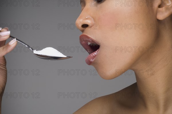 African woman eating spoon of sugar