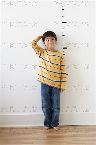 Asian boy standing next to height markers on wall