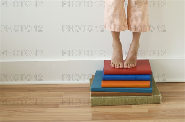 Girl standing on tiptoes on stack of books