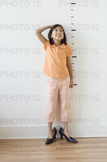 Asian girl wearing mother's shoes in front of height markers