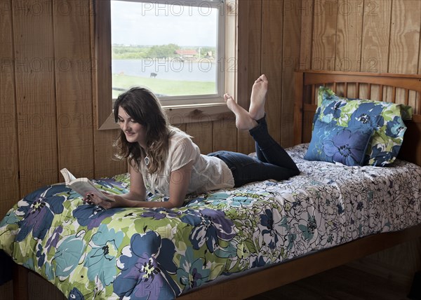 Caucasian woman reading on bed in dorm room