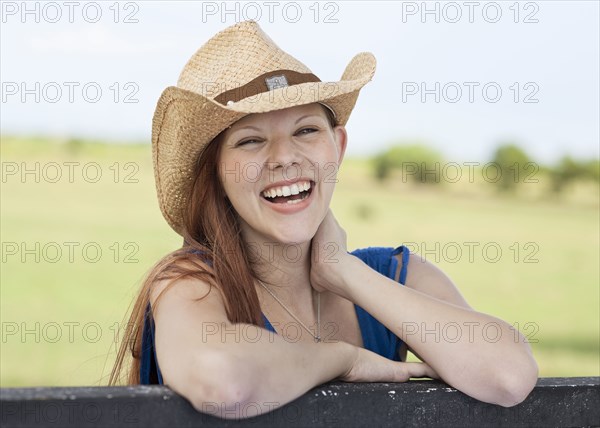 Caucasian woman laughing on fence in rural pasture