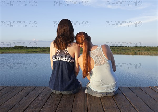 Caucasian women sitting on wooden dock over lake