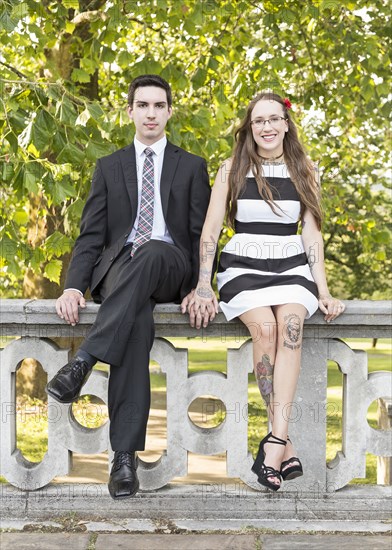 Well-dressed Caucasian couple sitting on wall at park