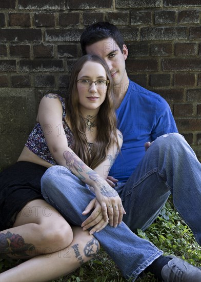 Caucasian couple sitting on ground leaning on wall
